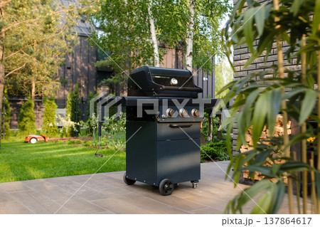 Grill set up in a backyard with trees and a building in the background during daytime in a residential area 137864617