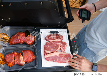 Grilling meat and checking temperature at outdoor barbecue event in backyard on sunny day with friends enjoying food preparation Grilling meat and checking temperature at outdoor barbecue event in backyard on sunny day with friends enjoying food preparation 137864626