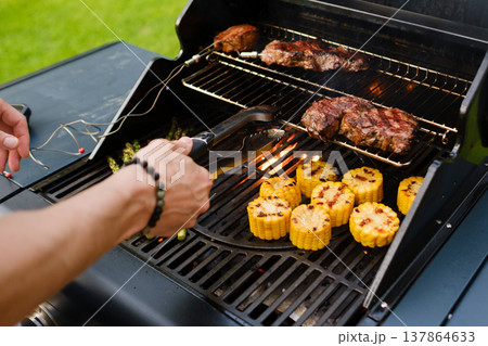 Grilling food on a barbecue with corn, asparagus, and steaks cooking outdoors during the day 137864633