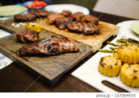 Grilled meat and vegetables served on wooden and stone plates with fresh ingredients arranged on the table at a gathering 137864638