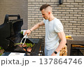 Cooking meat and vegetables on barbecue grill in backyard during sunny afternoon with friends nearby enjoying food and drinks 137864746