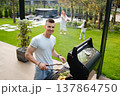 Man cooks on grill while friends enjoy time in yard during sunny day in backyard 137864750