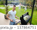 Man cooks on grill while friends enjoy time in yard during sunny day in backyard 137864751