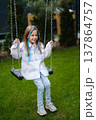 Young girl swings in backyard during a sunny afternoon, enjoying her time in a green garden while wearing casual clothes and smiling 137864757