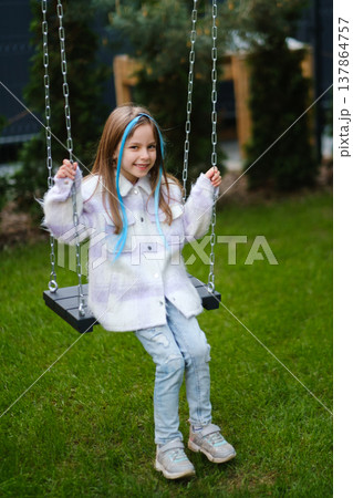 Young girl swings in backyard during a sunny afternoon, enjoying her time in a green garden while wearing casual clothes and smiling Young girl swings in backyard during a sunny afternoon, enjoying her time in a green garden while wearing casual clothes and smiling 137864757