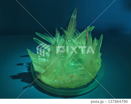 A close up view of sharp, translucent green crystals growing in a cluster, illuminated with dramatic lighting and casting shadows A close up view of sharp, translucent green crystals growing in a cluster, illuminated with dramatic lighting and casting shadows 137864790