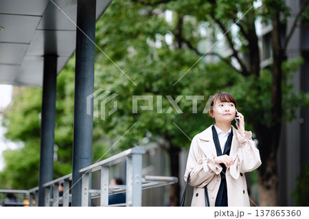 街中で携帯電話を使い通話する若いビジネスウーマン 街中で携帯電話を使い通話する若いビジネスウーマン 137865360