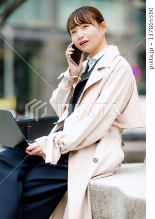 街中で携帯電話を使い通話する若いビジネスウーマン 街中で携帯電話を使い通話する若いビジネスウーマン 137865380