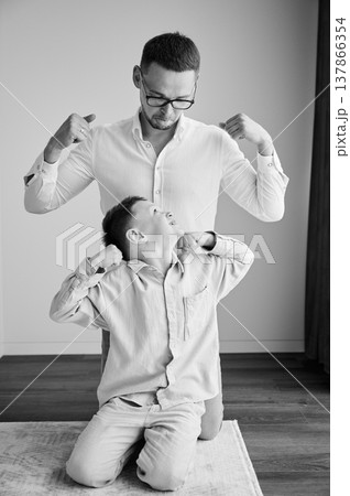 Young father playing with his curious son. Funny kid showing muscles to his dad. Family enjoying activity games at home. Black and white image. 137866354