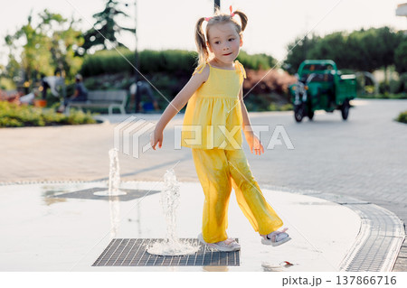 Cute little girl in yellow outfit playing in city fountain on summer day, happy childhood moment 137866716