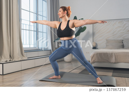 Yoga fitness workout training. Woman practicing yoga at home. Plus size female doing sports exercise on yoga mat indoor. Girl in sportswear have training workout for weight loss. Sport and fitness Yoga fitness workout training. Woman practicing yoga at home. Plus size female doing sports exercise on yoga mat indoor. Girl in sportswear have training workout for weight loss. Sport and fitness 137867259