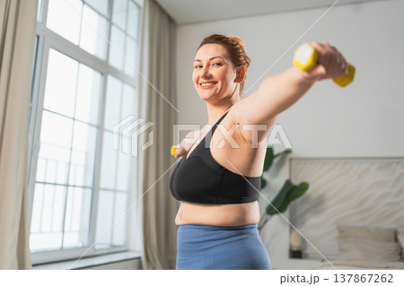 Fitness workout training. Woman picking up dumbbells. Plus size female doing sports exercise at home indoor. Girl in sportswear have workout weight training for weight loss. Sport and fitness Fitness workout training. Woman picking up dumbbells. Plus size female doing sports exercise at home indoor. Girl in sportswear have workout weight training for weight loss. Sport and fitness 137867262