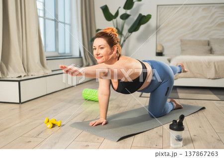 Yoga fitness workout training. Woman practicing yoga at home. Plus size female doing sports exercise on yoga mat indoor. Girl in sportswear have training workout for weight loss. Sport and fitness Yoga fitness workout training. Woman practicing yoga at home. Plus size female doing sports exercise on yoga mat indoor. Girl in sportswear have training workout for weight loss. Sport and fitness 137867263