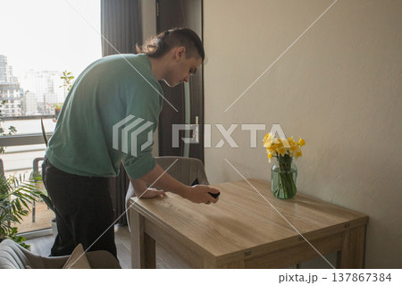 A man is wiping the surface of a wooden table in a well-lit room A man is wiping the surface of a wooden table in a well-lit room 137867384