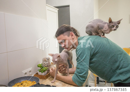 A man stands in a kitchen near a stove while a cat sits on his shoulder. A man stands in a kitchen near a stove while a cat sits on his shoulder. 137867385