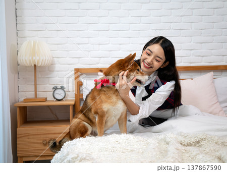 Smiling Asian woman bonding with Shiba Inu dog on bed in cozy bedroom. Happy pet and owner interaction, lifestyle concept of love, care, happiness and companionship in modern home Smiling Asian woman bonding with Shiba Inu dog on bed in cozy bedroom. Happy pet and owner interaction, lifestyle concept of love, care, happiness and companionship in modern home 137867590