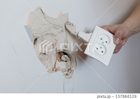 Electrician Removing Broken White Wall Socket from Cracked Plaster Exposing Wiring Inside Damaged Interior Room Wall Surface Electrician Removing Broken White Wall Socket from Cracked Plaster Exposing Wiring Inside Damaged Interior Room Wall Surface 137868129