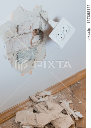 Damaged Wall With Broken Plaster Exposing Brick And Hanging Electrical Outlet Amidst Debris On Wooden Floor In Neutral Tones Damaged Wall With Broken Plaster Exposing Brick And Hanging Electrical Outlet Amidst Debris On Wooden Floor In Neutral Tones 137868135