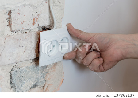 Electrician Installing White Double Socket Outlet On Exposed Brick Wall With Dusty Hand And Visible Wiring In Home Renovation Scene 137868137