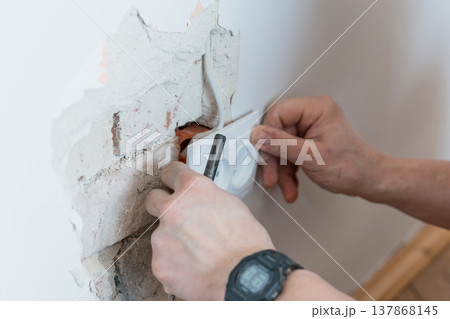 Electrician Installing Wall Socket in Damaged Concrete with Exposed Wires and Tools Showing White Outlet Against Rough Gray Texture Electrician Installing Wall Socket in Damaged Concrete with Exposed Wires and Tools Showing White Outlet Against Rough Gray Texture 137868145