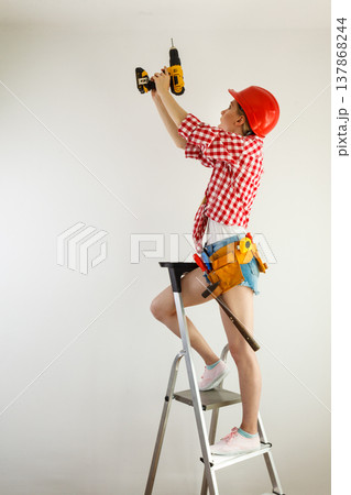 Woman using drill on ladder Woman using drill on ladder 137868244