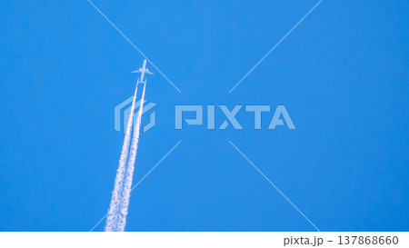 Airplane flying high in the sky leaving white trails during clear day with blue background Airplane flying high in the sky leaving white trails during clear day with blue background 137868660