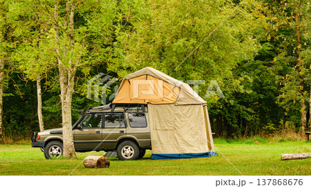 Camping setup with rooftop tent beside vehicle in grassy area during daytime in a natural setting 137868676