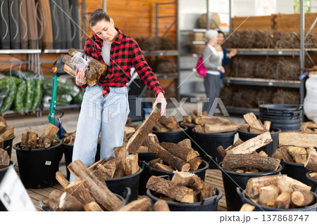 Young woman choosing firewood in store Young woman choosing firewood in store 137868747