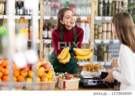 Young saleswoman giving bananas in grocery store 137868800