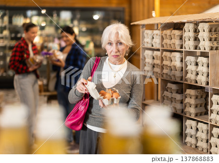 Elderly female customer selects and buys chicken eggs at grocery supermarket Elderly female customer selects and buys chicken eggs at grocery supermarket 137868883