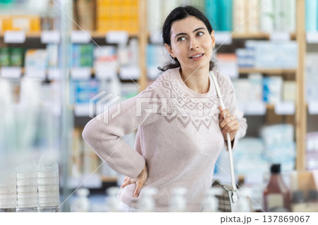 Woman holding her lower back in pharmacy Woman holding her lower back in pharmacy 137869067