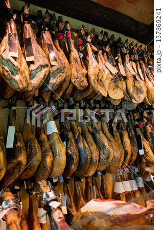 Row of dangling legs jamon with labels on showcase of butcher shop Row of dangling legs jamon with labels on showcase of butcher shop 137869241