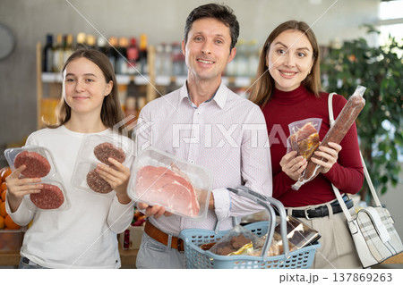 Dad, mom and daughter choose raw meat product and dry sausage in shop Dad, mom and daughter choose raw meat product and dry sausage in shop 137869263