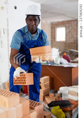 Builder in overall and hardhat carrying bricks in apartment Builder in overall and hardhat carrying bricks in apartment 137869292