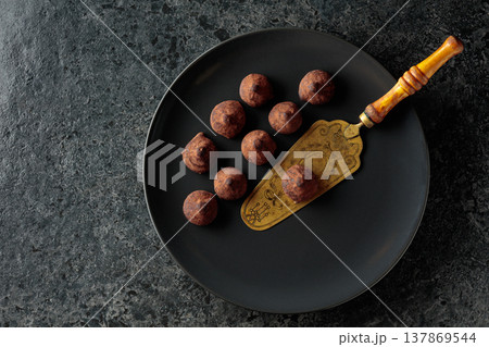 Chocolate truffles and vintage brass cake server on a black plate. 137869544
