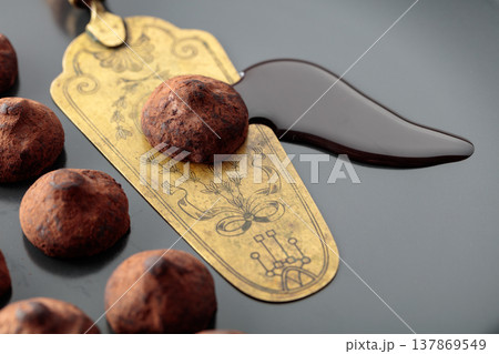 Chocolate truffles, chocolate sauce, and vintage brass cake server on a black plate. 137869549
