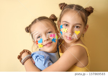 Kind friendly girls with a face decorated with pieces of colored puzzles. Children with autism hug each other, showing their love and care. 137869583
