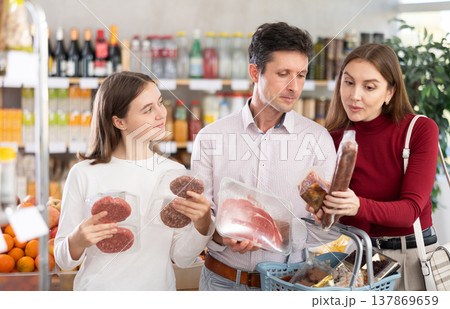 Dad, mom and daughter choose raw meat product and dry sausage in shop Dad, mom and daughter choose raw meat product and dry sausage in shop 137869659