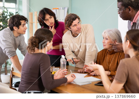 Businessman standing near table where colleagues talking and discussing ideas during business meeting in office Businessman standing near table where colleagues talking and discussing ideas during business meeting in office 137869660