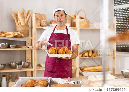 Caucasian male cook-baker worker with basket of croissant, shows many products Caucasian male cook-baker worker with basket of croissant, shows many products 137869665