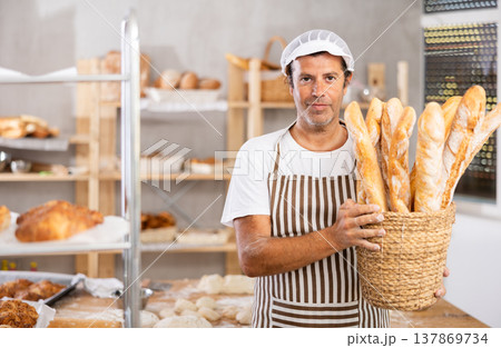 Caucasian male cook-baker worker with basket of baguettes, shows many products 137869734