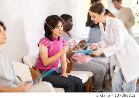 Group of people sitting in clinic queue while nurse speaking to girl Group of people sitting in clinic queue while nurse speaking to girl 137869812