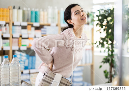 Girl suffers from back pain - looks for medicine in modern pharmacy Girl suffers from back pain - looks for medicine in modern pharmacy 137869833