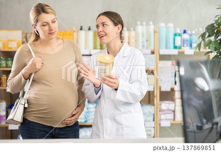 In drug store, pregnant woman examines formula for feeding, pharmacist consulting client In drug store, pregnant woman examines formula for feeding, pharmacist consulting client 137869851