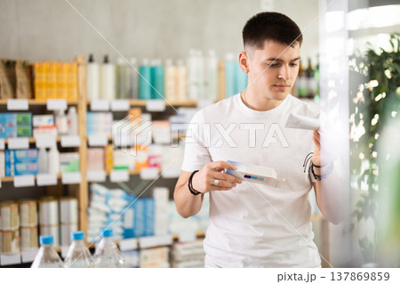Attentive young guy buyer choosing medical ointment and reading composition of medicine on box in pharmacy Attentive young guy buyer choosing medical ointment and reading composition of medicine on box in pharmacy 137869859