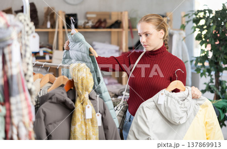 While shopping, teen girl browsing goods items and choose elect down jacket in store While shopping, teen girl browsing goods items and choose elect down jacket in store 137869913