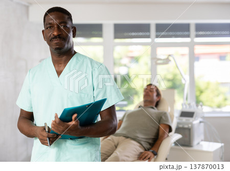 African American cosmetologist standing with clipboard in aesthetic medicine clinic 137870013
