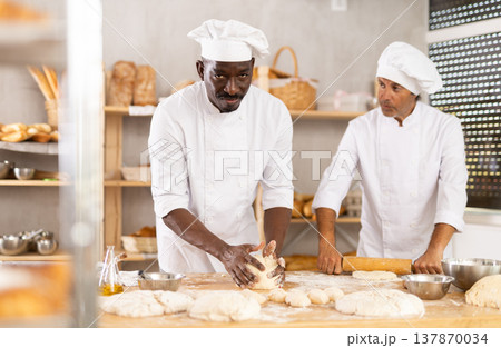 Two male bakers kneading dough and rolling it out Two male bakers kneading dough and rolling it out 137870034