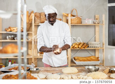 Male baker cutting raw dough with knife to make croissants or buns Male baker cutting raw dough with knife to make croissants or buns 137870058