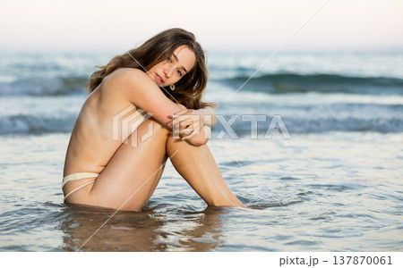 Semi naked young girl in bikini panties is sitting on sandy seashore 137870061